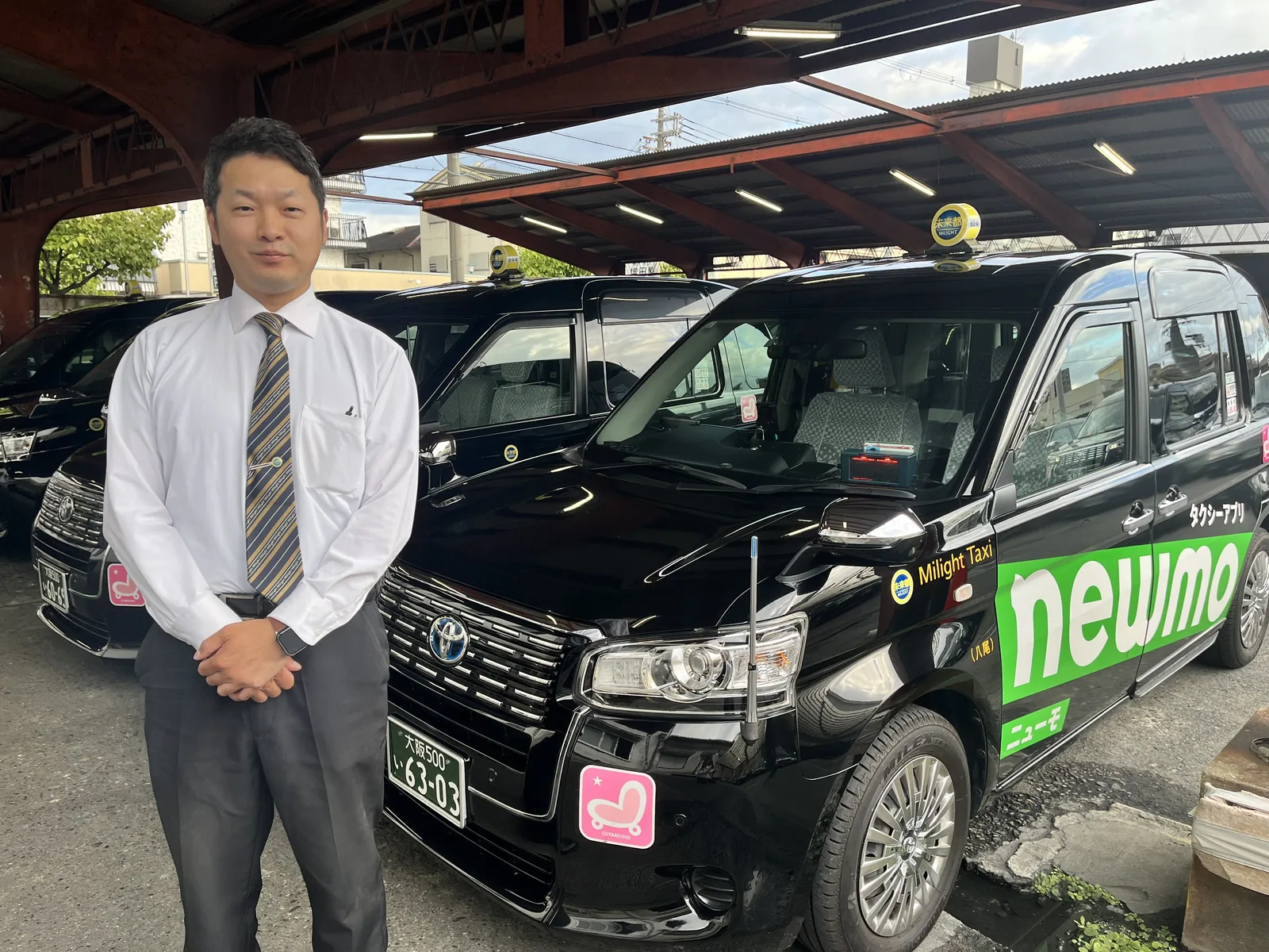 営業所の車庫でタクシーの前に立つY.T.さん