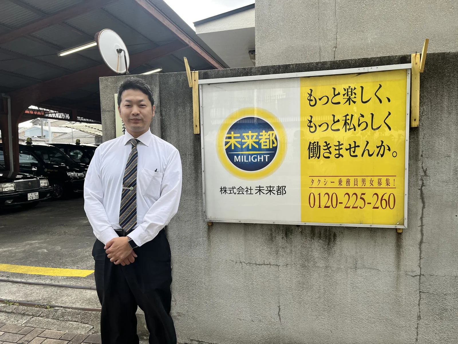 未来都の乗務員募集の看板の前に立つY.T.さん