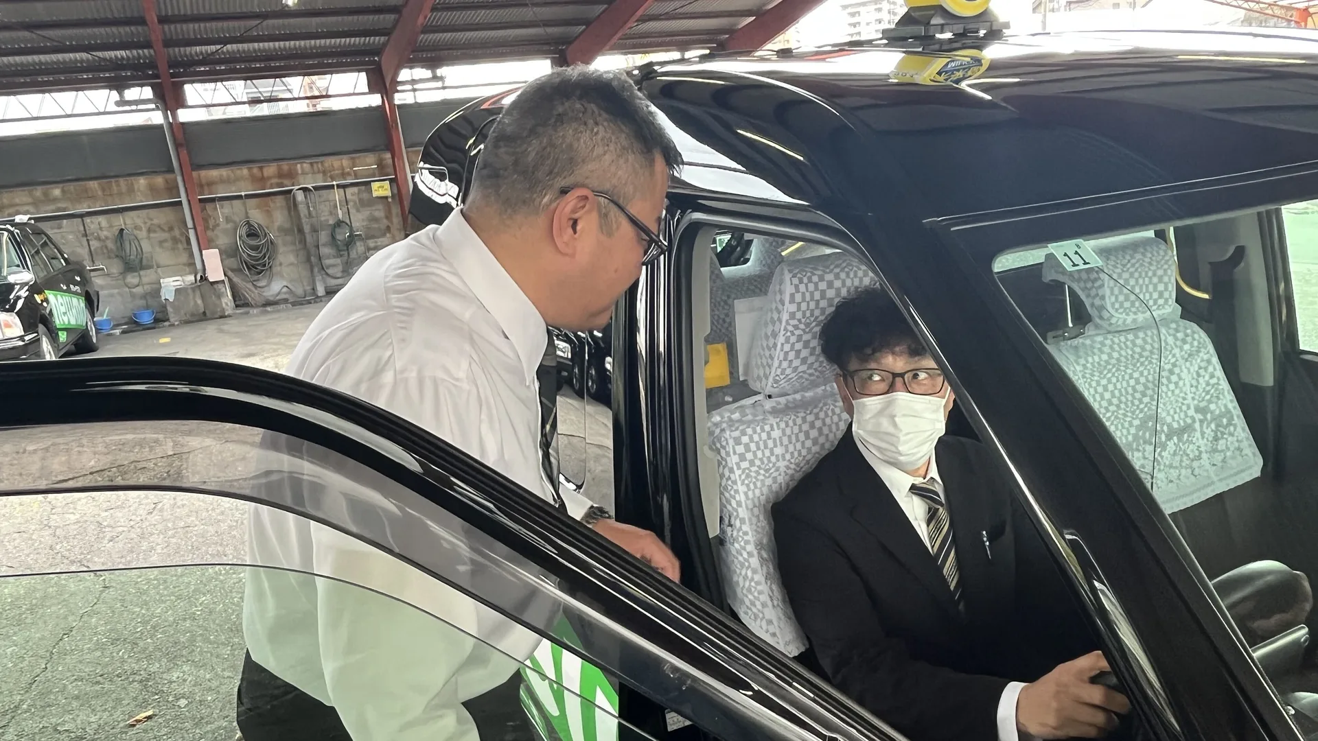車庫でタクシーの運転席に座る乗務員に声をかけるU.T.さん