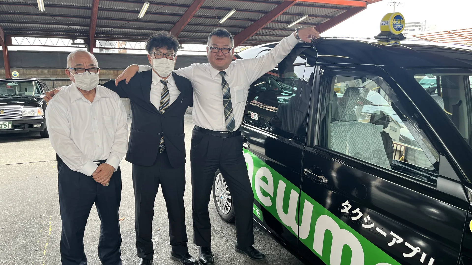 車庫のタクシーの前で、乗務員たちと肩を組んで並ぶU.T.さん