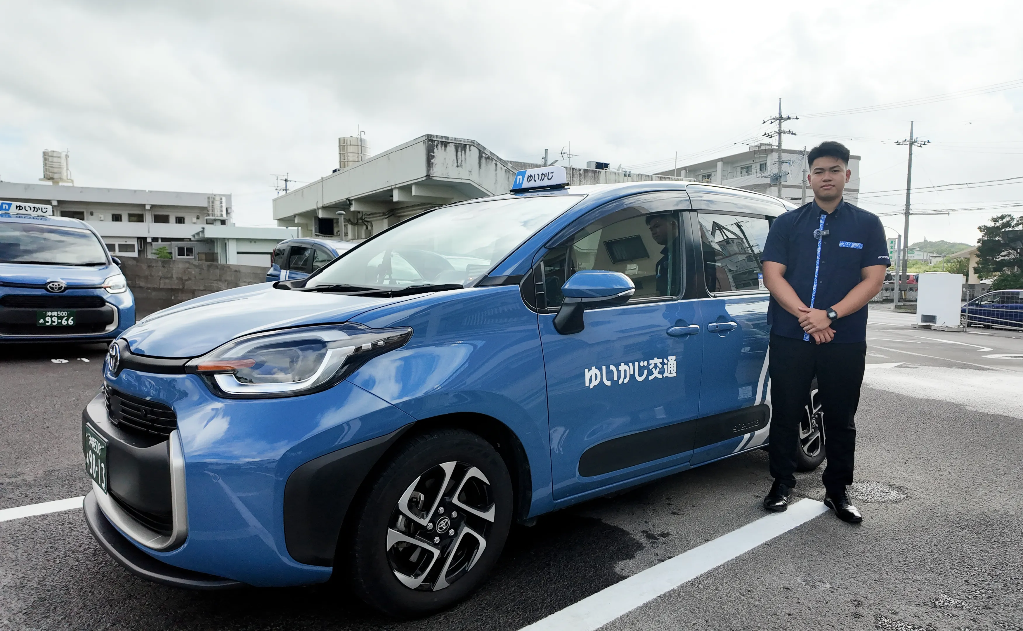営業所の駐車場でタクシーの横に立つS.R.さん